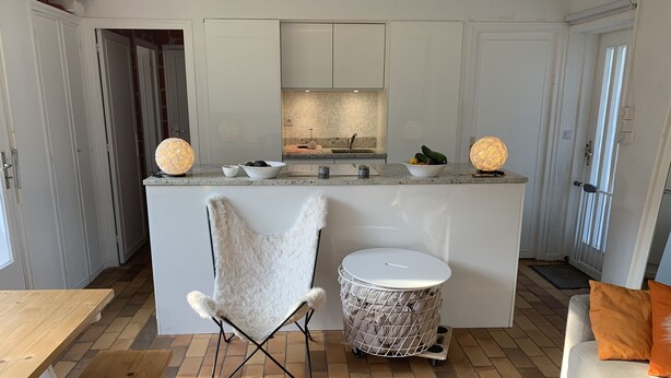 Une cuisine moderne dotée d’un îlot central, de meubles blancs et d’un coin salon accueillant avec une chaise et une petite table ronde.