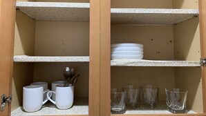 Ein Schrank mit Regalen, der weiße Tassen, einen Teller und klare Gläser beherbergt.