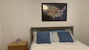 Ein Schlafzimmer mit einem Bett, einem Nachttisch, einer gerahmten Karte der USA und einer kleinen Vase mit Blumen.