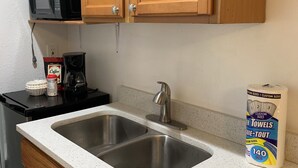 Eine Küche mit Spüle aus Edelstahl, Holzausbau, einer Kaffeemaschine und einer Packung Handtücher in Sondergröße.