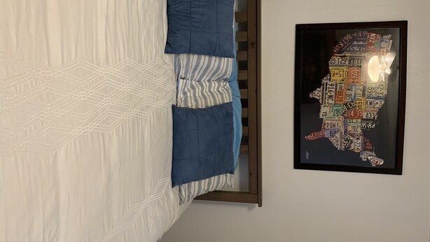 Ein Bett mit weißer Bettdecke und blauen Kissen, ein Holz-Kopfstück und eine an der Wand hängende Karte der Vereinigten Staaten.