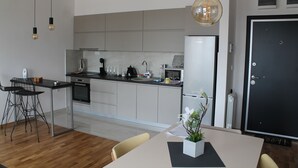Una cucina moderna con isola centrale, sgabelli da bar, un tavolo da pranzo con un vaso di fiori, illuminazione a sospensione e una porta con cornice nera.