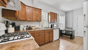 Una cocina con armarios de madera, estufa a gas, lavavajillas y encimera con distintos utensilios de cocina.
