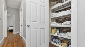 Un pasillo con piso de madera, una puerta blanca y un área de almacenamiento con estanterías y cajas.