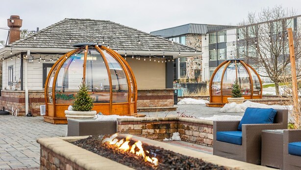 Een terras met een vuurkuil, buitenmeubels en een overdekt zitgedeelte met uitzicht op een gebouw.