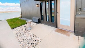 Een modern huis met een grote glazen deur, een klein terras en uitzicht op een meer.