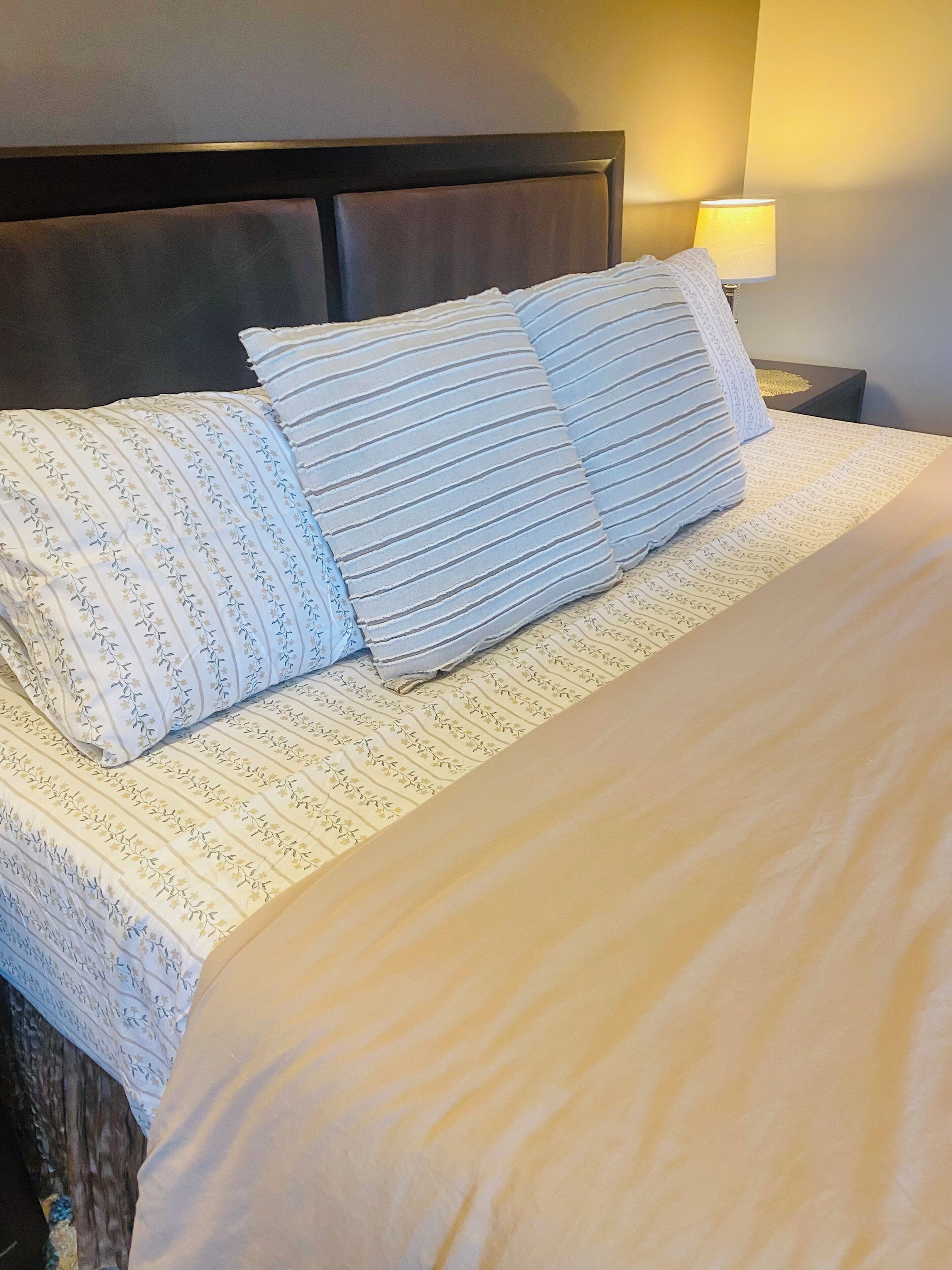Una cama bien hecha con almohadas a rayas y una colcha estampada con motivos florales.