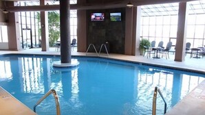 Een binnenzwembad met helder water, een zwembadtrap en een televisiescherm aan de muur.