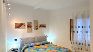 A bedroom with a bed, a chair, a nightstand, and wall art. - Centralissimo Casa Piazzetta (Siena)