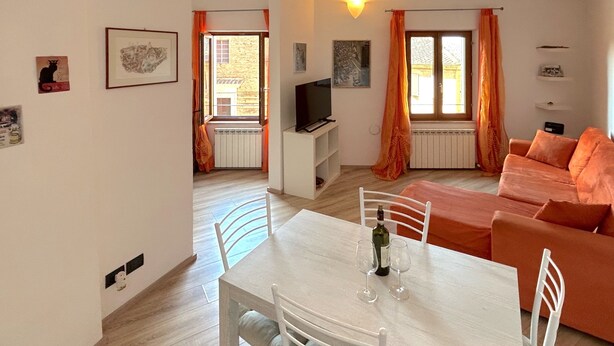 A modern living room with a white table, orange sofa, and a TV on a stand. - Centralissimo Casa Piazzetta (Siena)