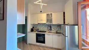 A compact kitchen with white cabinets, a stainless steel refrigerator, and a tiled backsplash. - Centralissimo Casa Piazzetta (Siena)