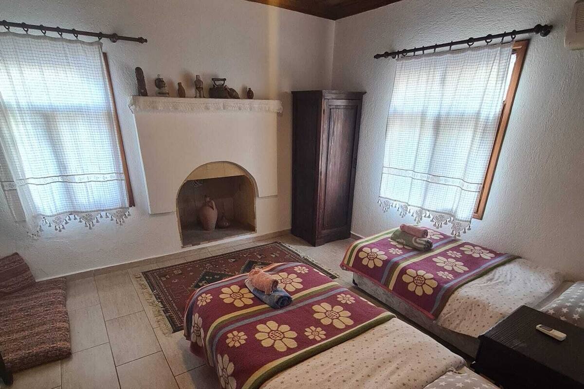 A cozy bedroom with two beds, a fireplace, and a wooden ceiling.