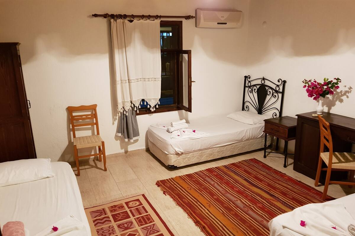 A bedroom with a bed, a desk, a chair, a wardrobe, and a window with curtains.