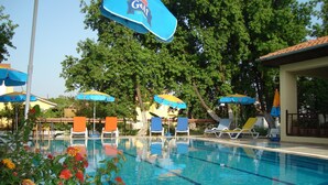 Ein Pool mit Liegestühlen und Sonnenschirmen, umgeben von Bäumen und einem Gebäude.