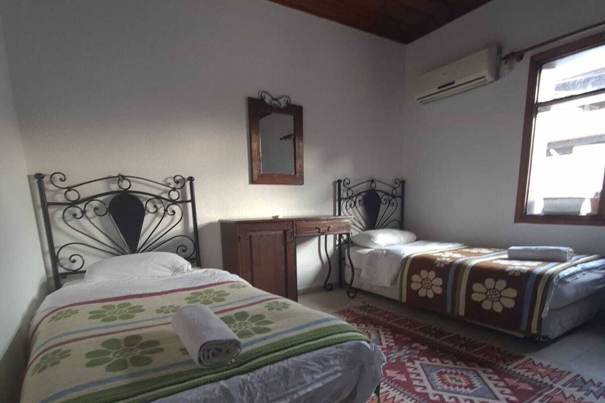 A bedroom with two beds, a wooden ceiling, a mirror, and a window.