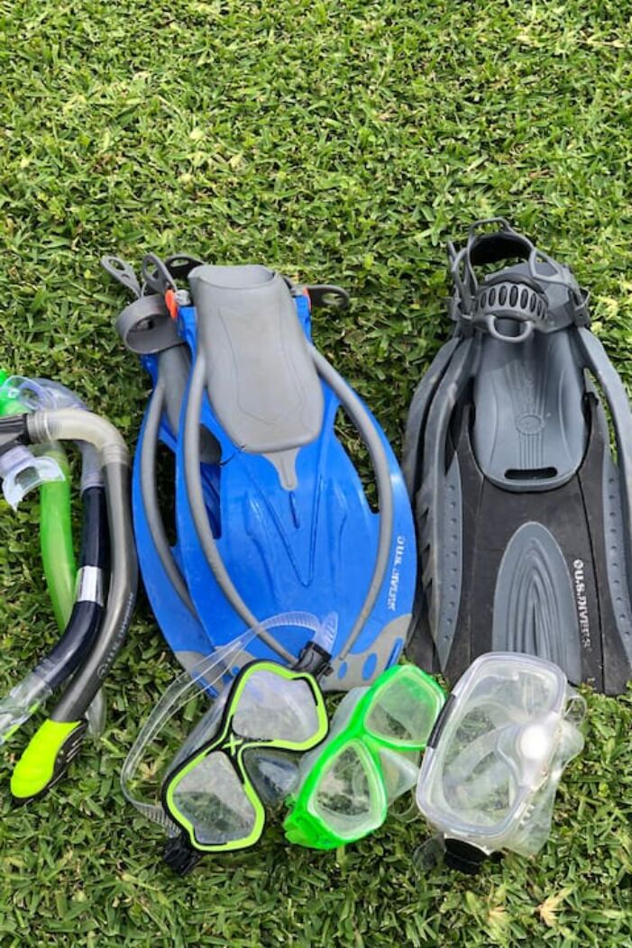 Un juego de snorkel azul, aletas negras y máscaras de snorkel verdes sobre césped.