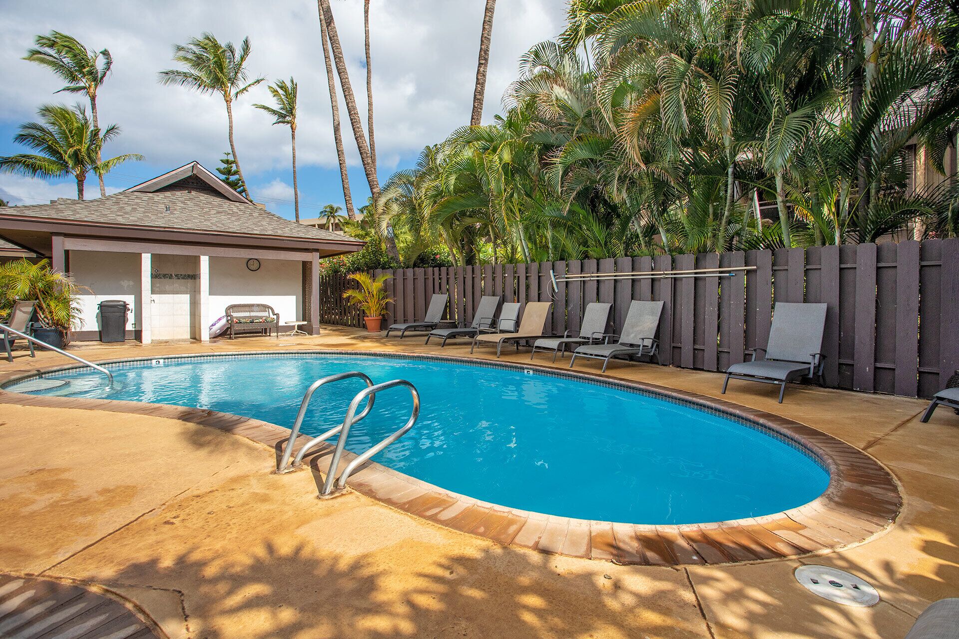 A swimming pool with lounge chairs and a covered seating area, surrounded by palm trees.