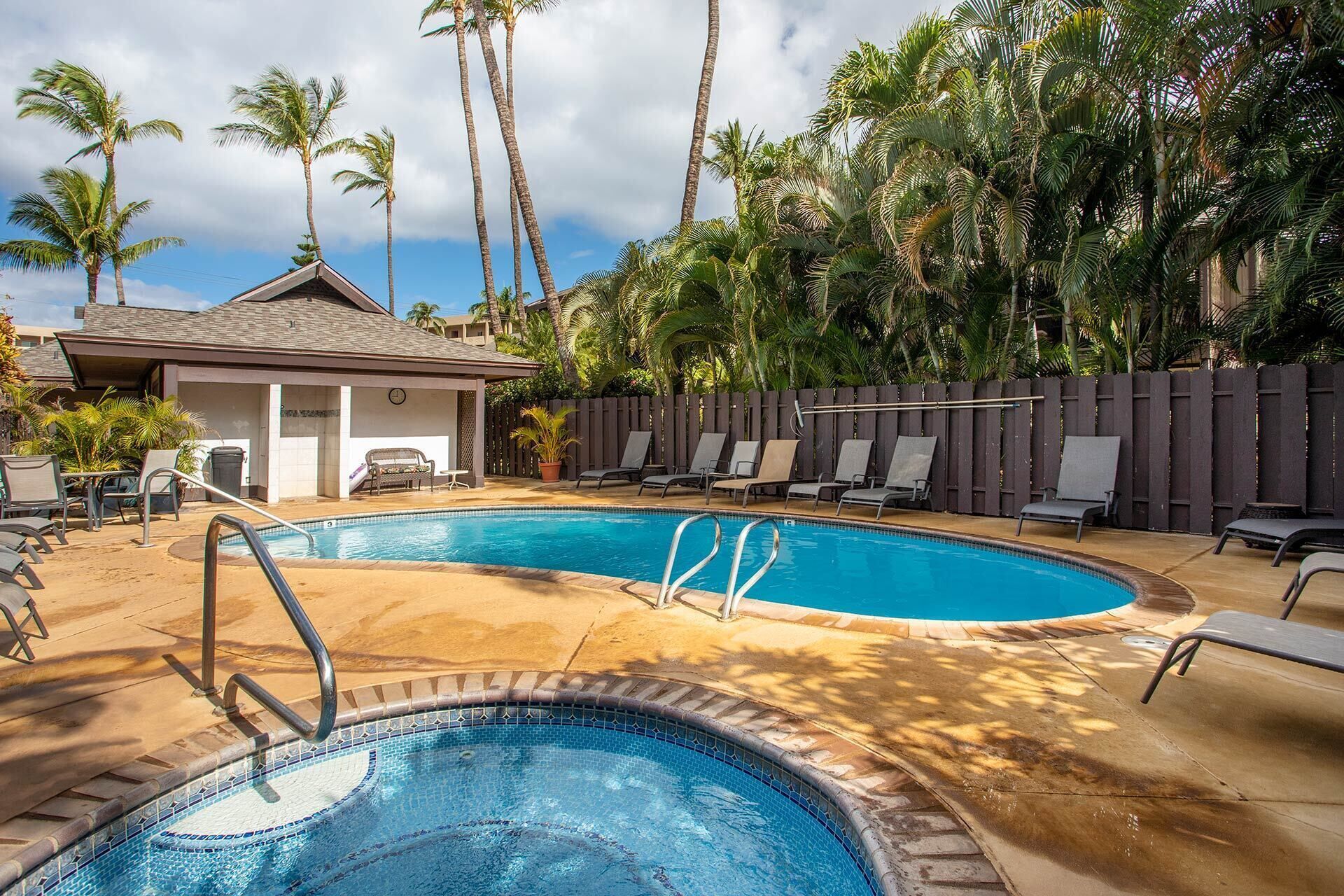 A swimming pool with lounge chairs and a covered seating area, surrounded by palm trees.