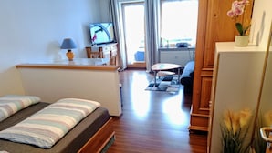 Kompakti hotellihuone, jossa on sänky, pieni työpöytä, televisio ja näkymä ulos.