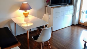 Moderni olohuone, jossa on ruokapöytä, lamppu, televisio ja valkoinen kaappi.