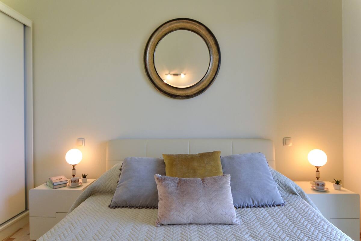A neatly arranged bedroom with a bed, pillows, bedside tables, and wall-mounted lamps.