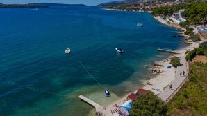 Un pueblo costero con aguas azul turquesa, barcos y una playa con gente y edificios.