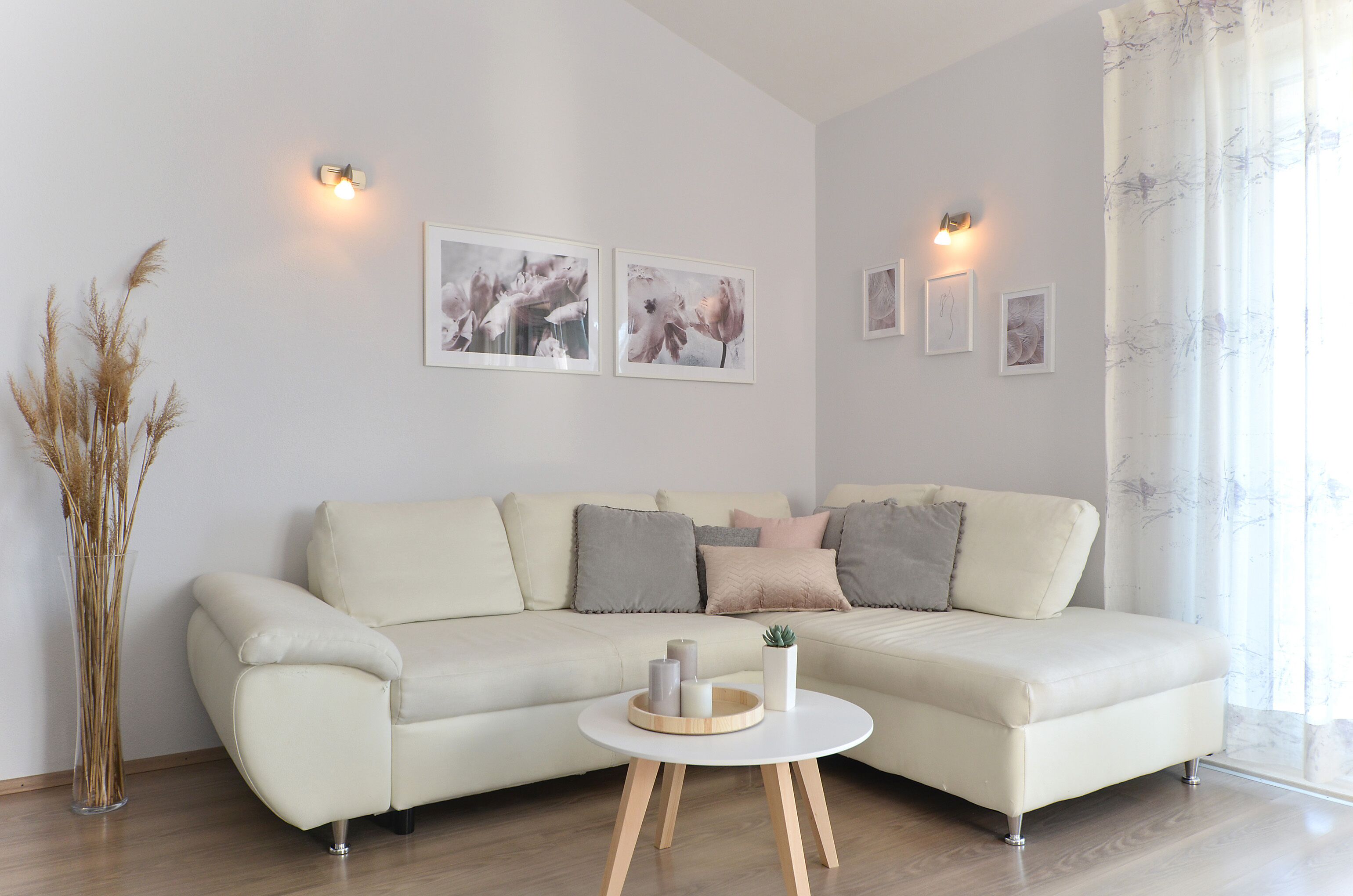 A modern living room with a cream-colored sofa, a round coffee table with candles, and wall-mounted picture frames.