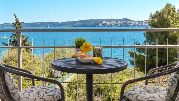 Un balcón con una mesa lista para dos personas, con vistas a una extensión de agua y una costa lejana.