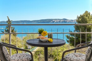 Un balcón con una mesa lista para dos personas, con vistas a una extensión de agua y una costa lejana.