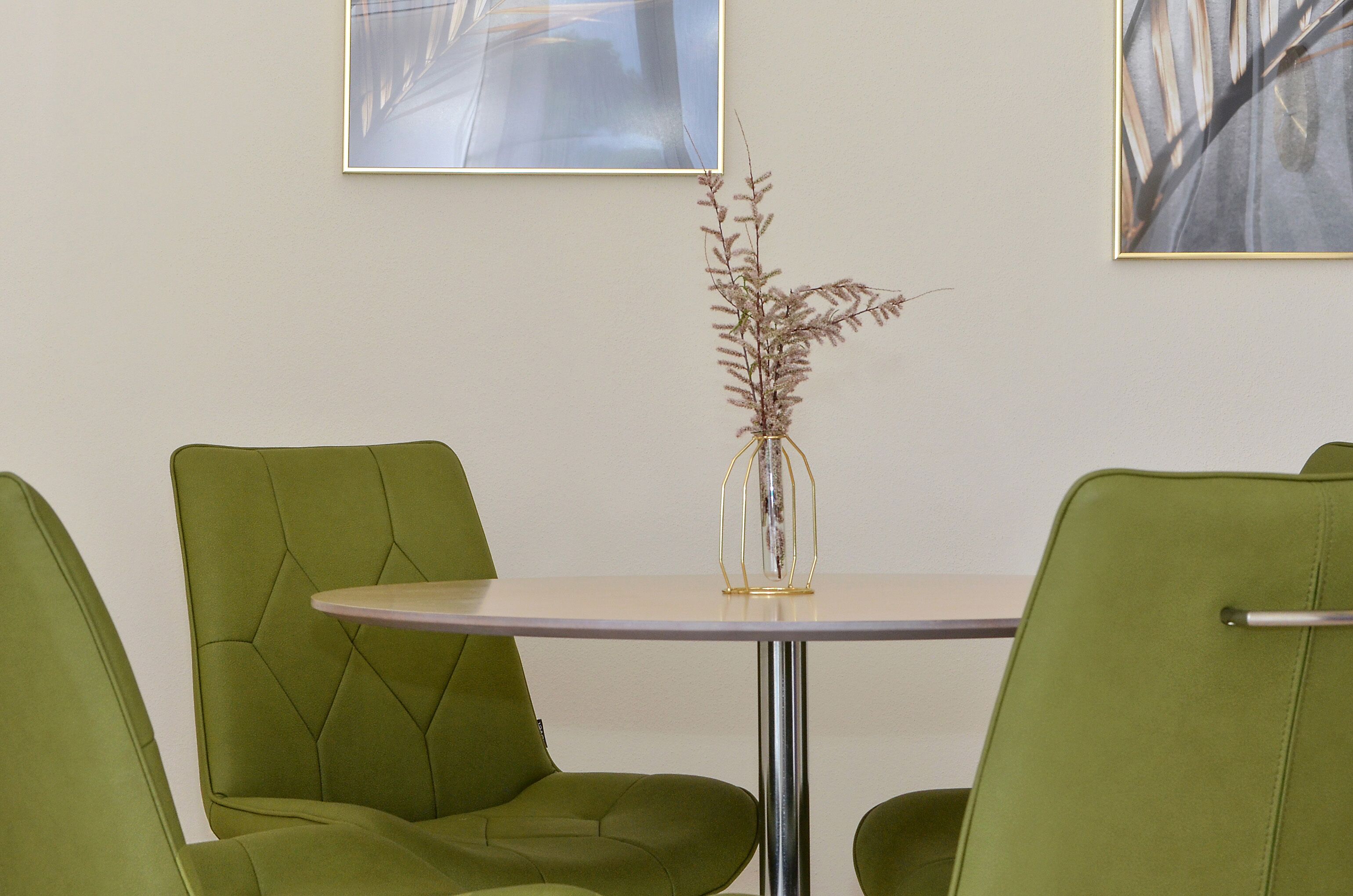A round table with a vase of dried plants, surrounded by four green chairs.