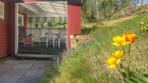 Ein rotes Gebäude mit einer Veranda, einem Essbereich mit Plastikstühlen und einem Garten mit gelben Tulpen und violetten Blumen.