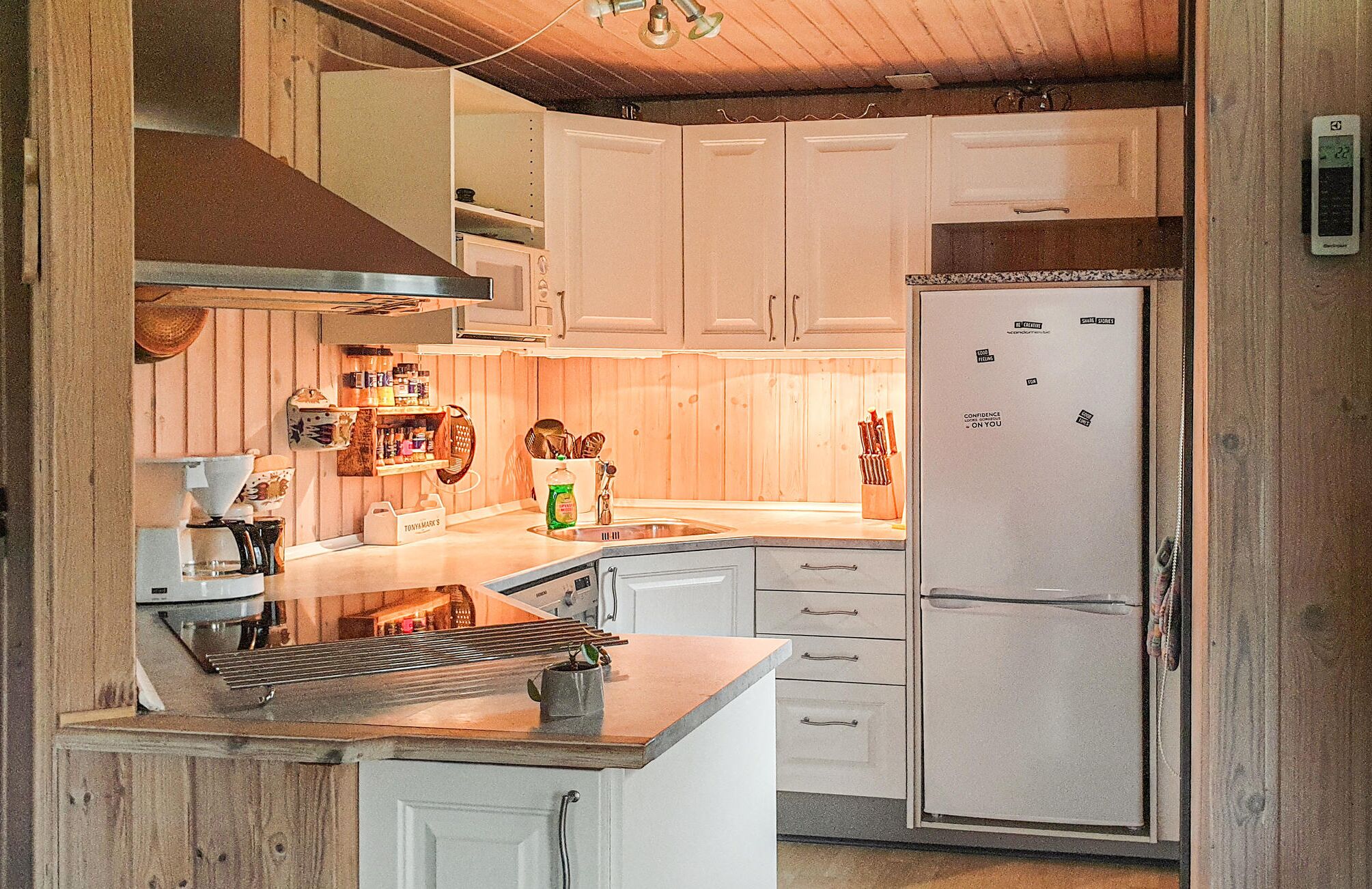 Cozinha compacta com armários brancos, micro-ondas embutido e geladeira decorada com imãs.