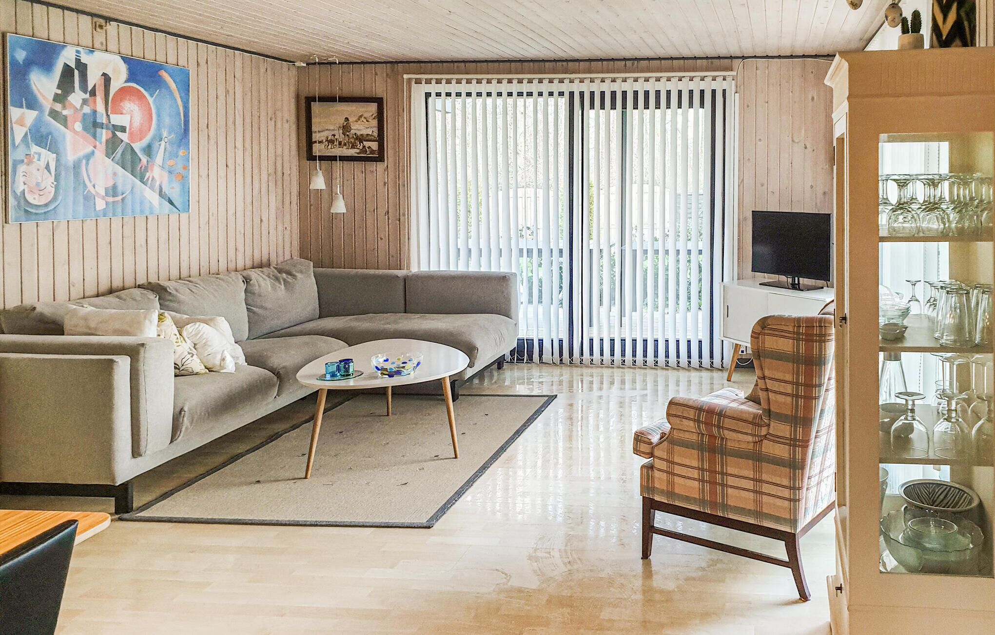 A living room with a sofa, a coffee table, a plaid armchair, a TV, and a glassware display.
