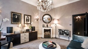 A modern living room with a chandelier, fireplace, framed artwork, and a television. - Cadogan Square - 1 bed (London)