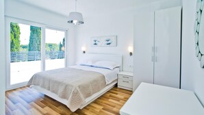 Un dormitorio con cama, mesitas de noche, armario y un amplio ventanal con vistas al verdor.