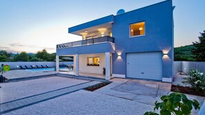 Una casa moderna de dos pisos con un porche cubierto, una piscina y un garaje.