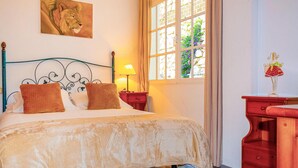 Una camera da letto con un letto, un comodino, una lampada, una finestra con tende e un quadro raffigurante un leone, oltre a una cassettiera.