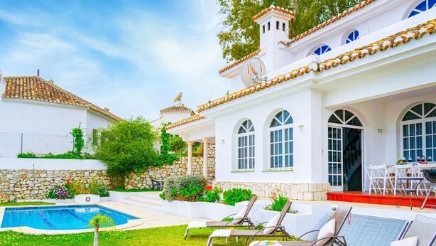 Una villa bianca con piscina, area salotto esterna e un muro in pietra.