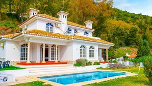 Una villa bianca con piscina, ampie finestre e un giardino.