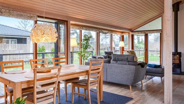 Ett rymligt rum med ett träpanelat tak, en matplats med bord och stolar, en grå soffa och en öppen spis.