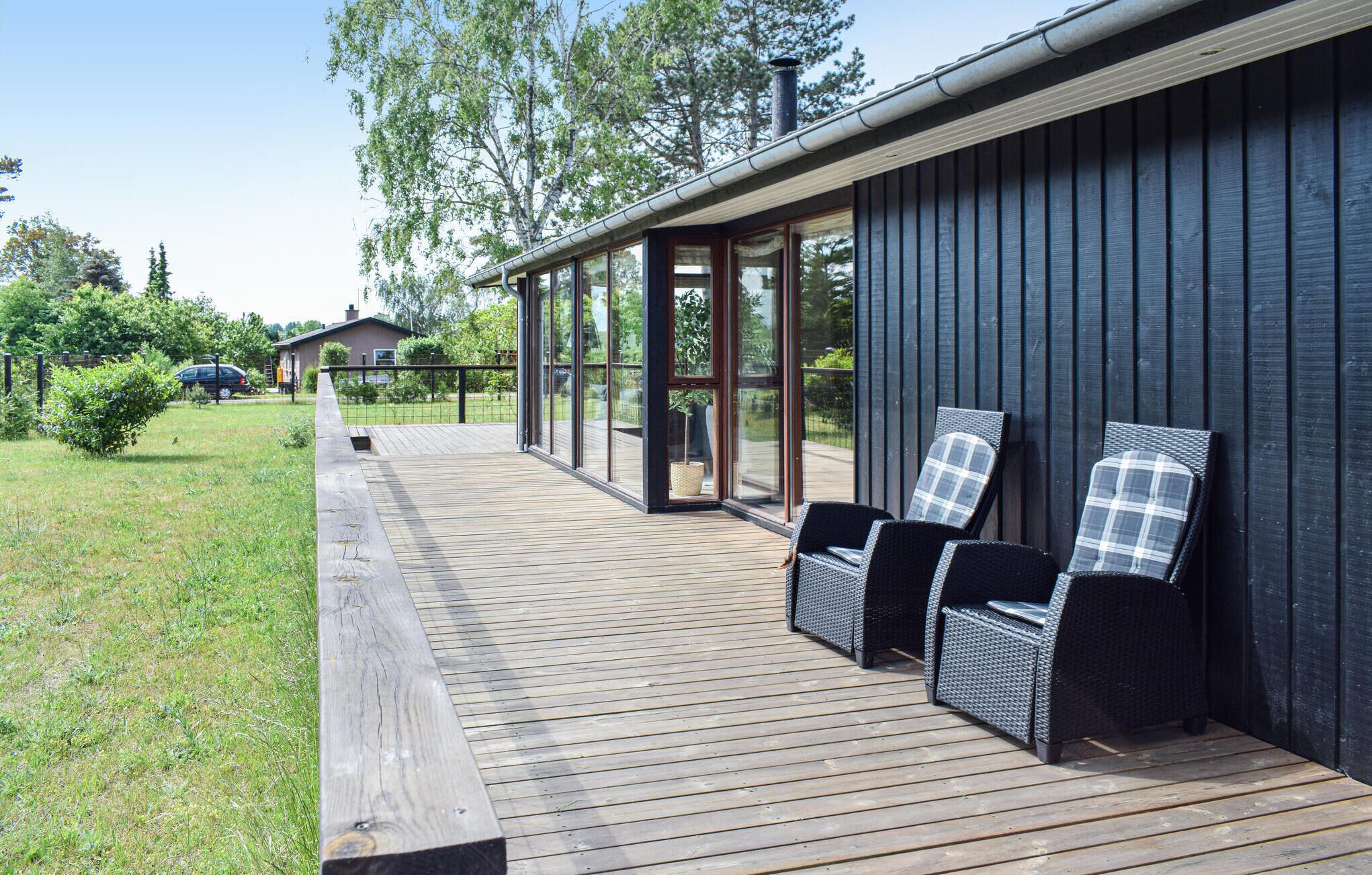 A wooden deck with wicker chairs, a glass-enclosed patio, and a dark wooden building facade.