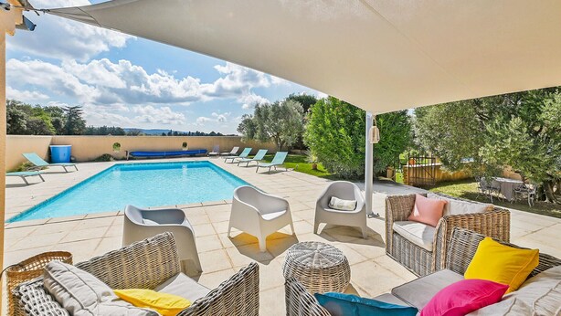 Un espace aménagé au bord de la piscine, comprenant une piscine, des chaises longues et un coin salon abrité.