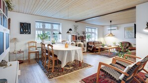 A spacious living room with a dining area, wooden ceiling, large windows, and a bookshelf. - 3 bedroom awesome home in Ringkøbing (Lem St)