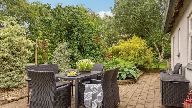 An outdoor patio with wicker furniture, a table with a fruit bowl, and a variety of plants and trees. - 3 bedroom awesome home in Ringkøbing (Lem St)