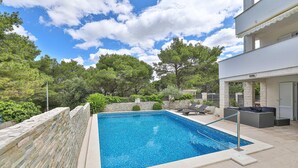 A rectangular swimming pool with a tiled edge, surrounded by a stone wall and a stone pathway.