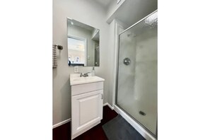 Bathroom features a large mirror above a vanity with a sink and cabinet, and a glass shower enclosure.