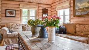 Acogedor interior de una cabaña de troncos con una mesa de madera, dos sofás y ventanas amplias.