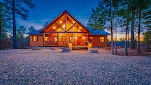 A log cabin with a prominent front porch, large windows, and a symmetrical roof design.