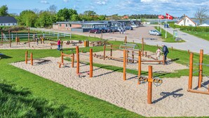 Un patio de juegos al aire libre con diverso equipo de ejercicio, un estacionamiento con coches y un edificio con señalización.