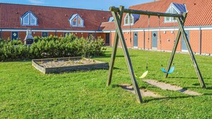 Un parque infantil con columpios y un edificio de ladrillo con ventanas al fondo.